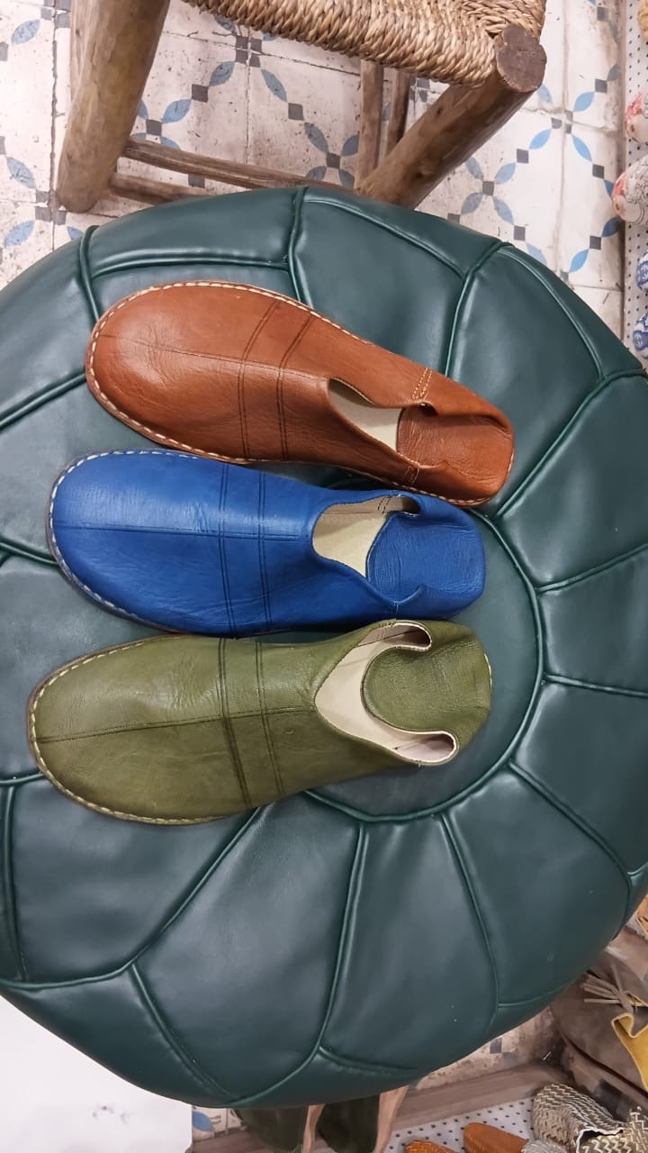 Hand-stitched Moroccan leather slippers resting on a leather pouf